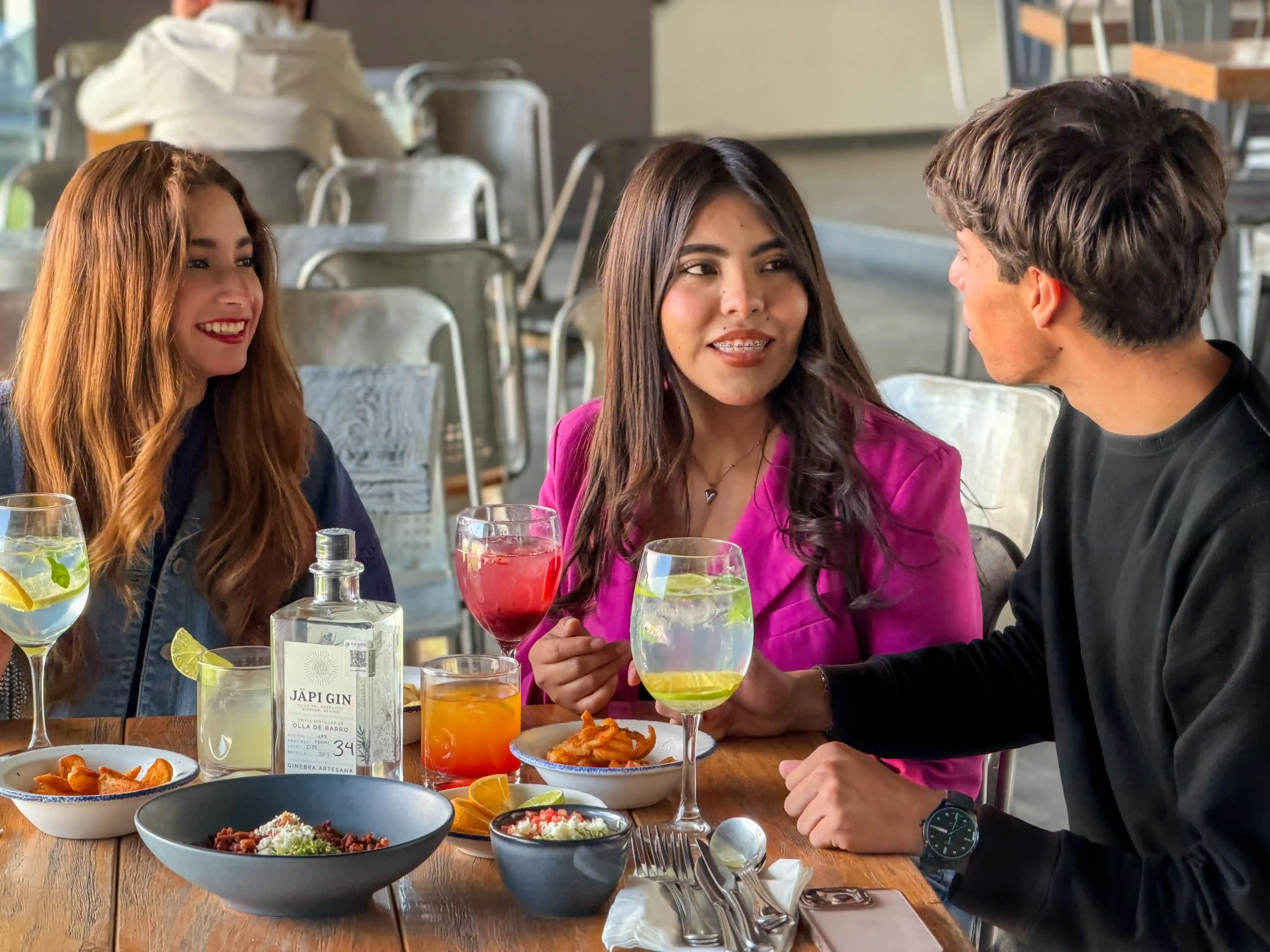 Grupo de tres personas conviviendo en mesa con cócteles y entradas